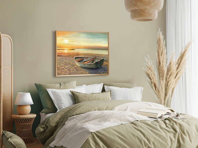Op de afbeelding: Een rechthoekige ingelijste wandkunstprint met een landschapsschilderij van een kleine roeiboot die bij zonsondergang op een zandstrand ligt. De sc&egrave;ne toont een kalme oceaanhorizon met een felle zon, een zachte oranje lucht en een houten boot.
