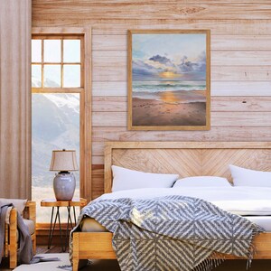 May include: A rectangular framed wall art print featuring a coastal landscape painting. The artwork depicts a sunset over the ocean with soft clouds, gentle waves washing onto a sandy beach, and golden light reflecting on the wet sand and water.