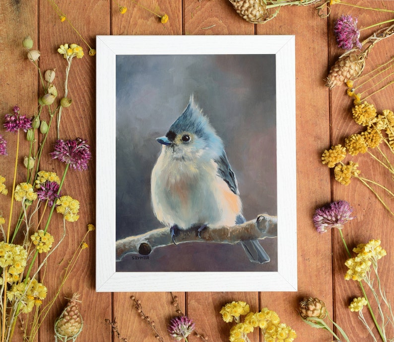May include: A framed painting of a blue-gray bird with a crested head perched on a branch. The bird is painted in a realistic style with soft, muted colors. The background is a soft gray.
