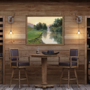 Pode incluir: Uma &aacute;rea de bar em madeira com duas cadeiras girat&oacute;rias de assento castanho escuro, uma mesa redonda central com pedestal e duas estantes altas. Uma pintura de paisagem emoldurada de um rio ao p&ocirc;r do sol est&aacute; pendurada na parede entre dois candeeiros de parede em forma de chifre.