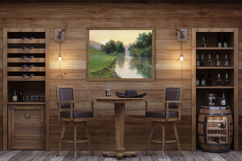 Pode incluir: Uma &aacute;rea de bar em madeira com duas cadeiras girat&oacute;rias de assento castanho escuro, uma mesa redonda central com pedestal e duas estantes altas. Uma pintura de paisagem emoldurada de um rio ao p&ocirc;r do sol est&aacute; pendurada na parede entre dois candeeiros de parede em forma de chifre.
