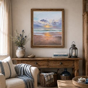 May include: A square framed oil painting depicting a sunset over a calm ocean beach with soft clouds, golden light reflecting on the wet sand and water, displayed on a wall above a wooden console table in a room with a chair and decor.