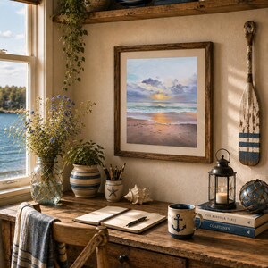 May include: A framed painting of a sunset over a beach hangs on a wall above a wooden desk. The desk features a ceramic mug with an anchor design, a notebook, a lantern, a seashell, and a vase with blue flowers. A wooden oar hangs nearby.