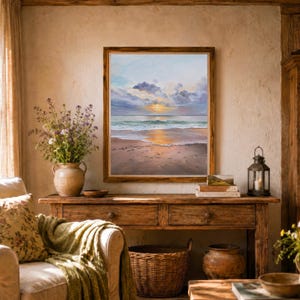 May include: A framed wall art print depicting a coastal sunset scene with a sandy beach, gentle ocean waves, and a cloudy sky. The painting features soft hues of orange, blue, and grey, capturing the reflection of the sun on the wet sand.