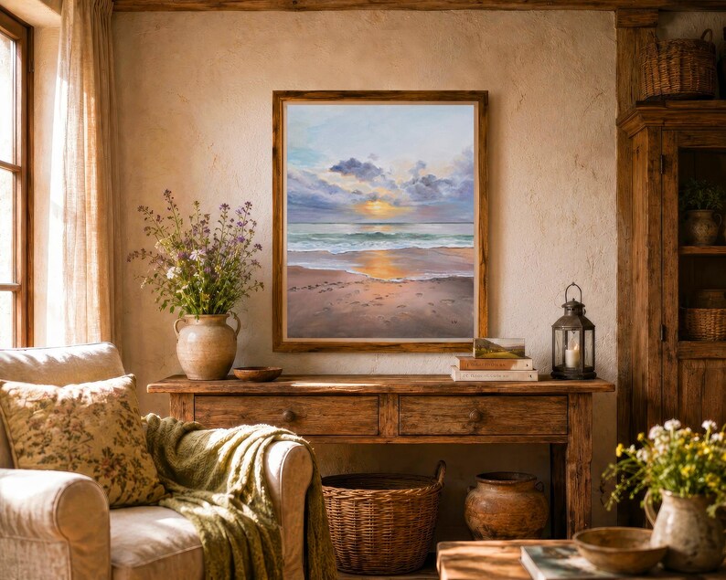 May include: A framed wall art print depicting a coastal sunset scene with a sandy beach, gentle ocean waves, and a cloudy sky. The painting features soft hues of orange, blue, and grey, capturing the reflection of the sun on the wet sand.