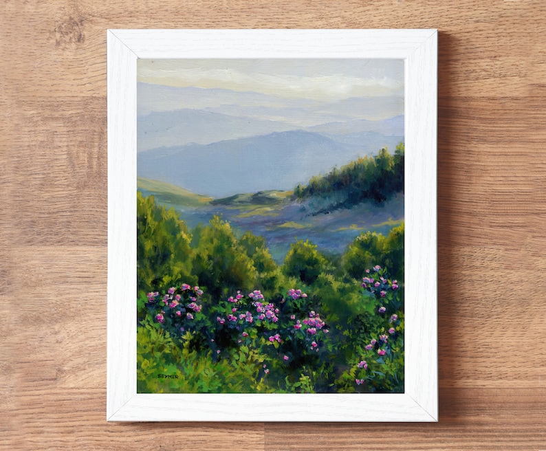 May include: A framed oil painting depicting a landscape with vibrant green bushes and clusters of pink flowers in the foreground, leading to rolling blue mountains in the distance under a soft sky. The signature STYNER is visible in the bottom left.