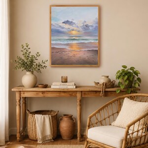 May include: A rectangular framed painting depicting a beach scene at sunset with soft clouds, a golden sun reflecting on the water, and wet sand in the foreground. The artwork features a palette of light blue, soft purple, and warm golden tones.