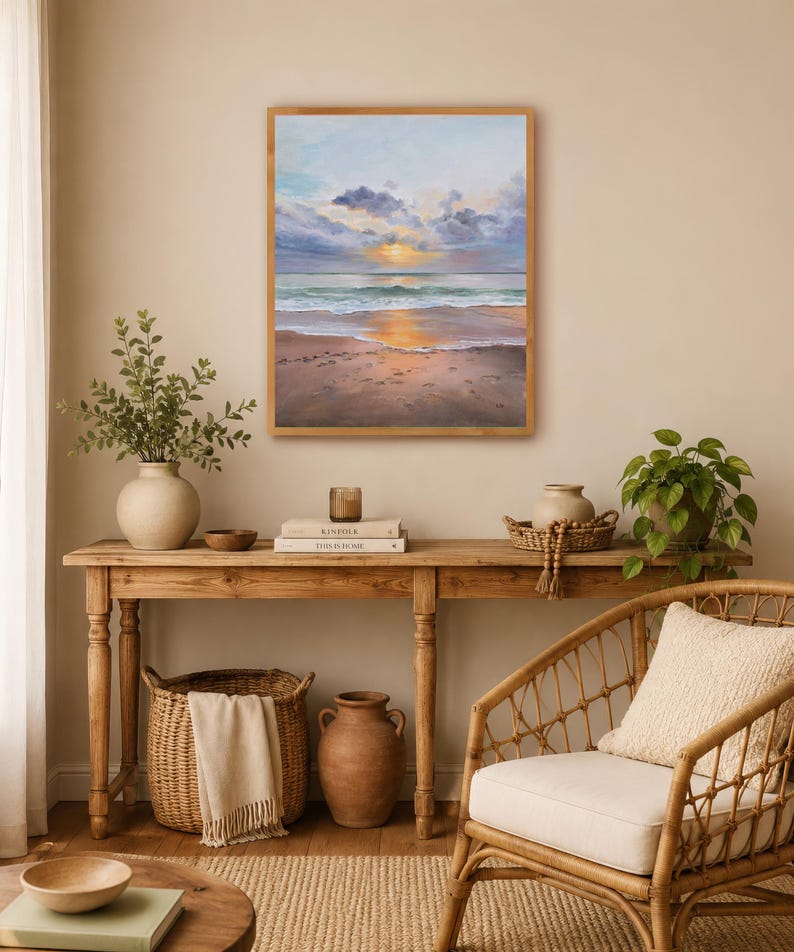 May include: A rectangular framed painting depicting a beach scene at sunset with soft clouds, a golden sun reflecting on the water, and wet sand in the foreground. The artwork features a palette of light blue, soft purple, and warm golden tones.