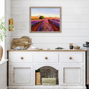 May include: A painting of a lavender field with a winding path leading to a small tree in the distance. The field is a vibrant purple and the sky is a soft blue. The painting is framed in a light wood frame.