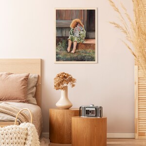 May include: A painting of a young girl sitting on a porch step, holding a white rabbit close to her chest. She is wearing a green dress and has red hair. The painting is framed in a light wood frame.