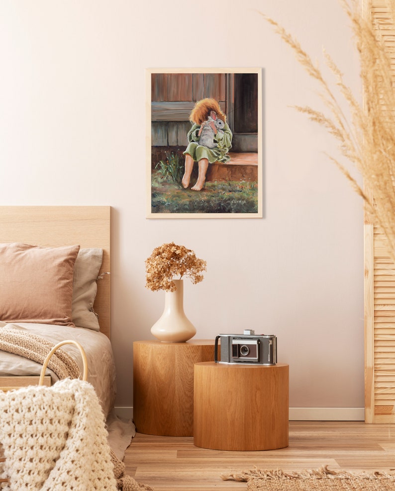 May include: A painting of a young girl sitting on a porch step, holding a white rabbit close to her chest. She is wearing a green dress and has red hair. The painting is framed in a light wood frame.