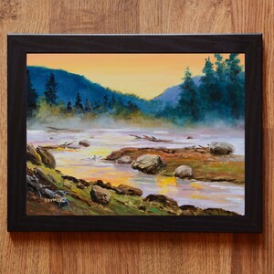 May include: An oil painting in a black frame depicting a river landscape at sunset. The scene features dark blue mountains, evergreen trees, and a misty river with rocks and driftwood. The sky is a warm orange, and the artist signature SEYMER is visible in the lower left corner.