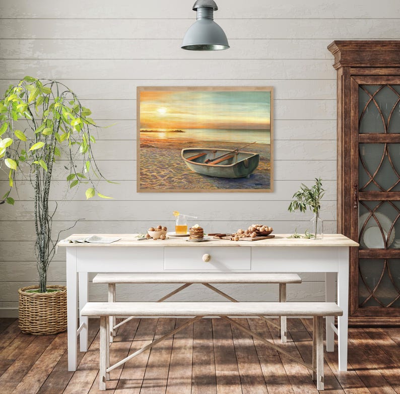 Op de afbeelding: Een rechthoekige wandkunstprint met een landschapsschilderij van een kleine roeiboot die bij zonsondergang op een zandstrand ligt. De sc&egrave;ne toont zachte oranje en gele tinten in de lucht die reflecteren op het kalme water van de zee.
