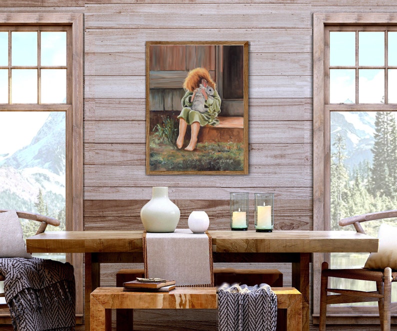 May include: A painting of a young girl in a green dress holding a white rabbit. The girl is sitting on a wooden porch with a wooden railing. The painting is framed in a gold frame.