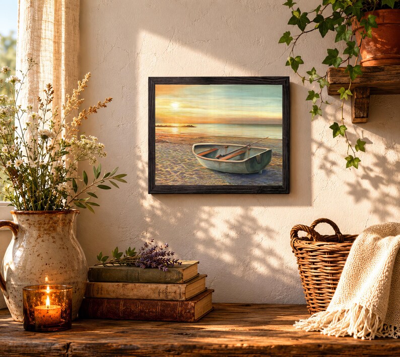 Op de afbeelding: Een ingelijste kunstdruk met een kleine roeiboot op een zandstrand bij zonsondergang. De sc&egrave;ne toont een rustige oceaanhorizon onder een zachte gouden lucht, met de boot op de voorgrond. Het kunstwerk is geplaatst in een donkere lijst.