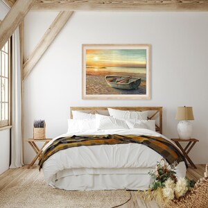 Op de afbeelding: Een rechthoekige ingelijste wandkunstprint met een schilderij van een kleine roeiboot die bij zonsondergang op een zandstrand ligt. De sc&egrave;ne toont een rustige kustlijn met een gloeiende oranje zon aan de horizon en houten roeispanen.