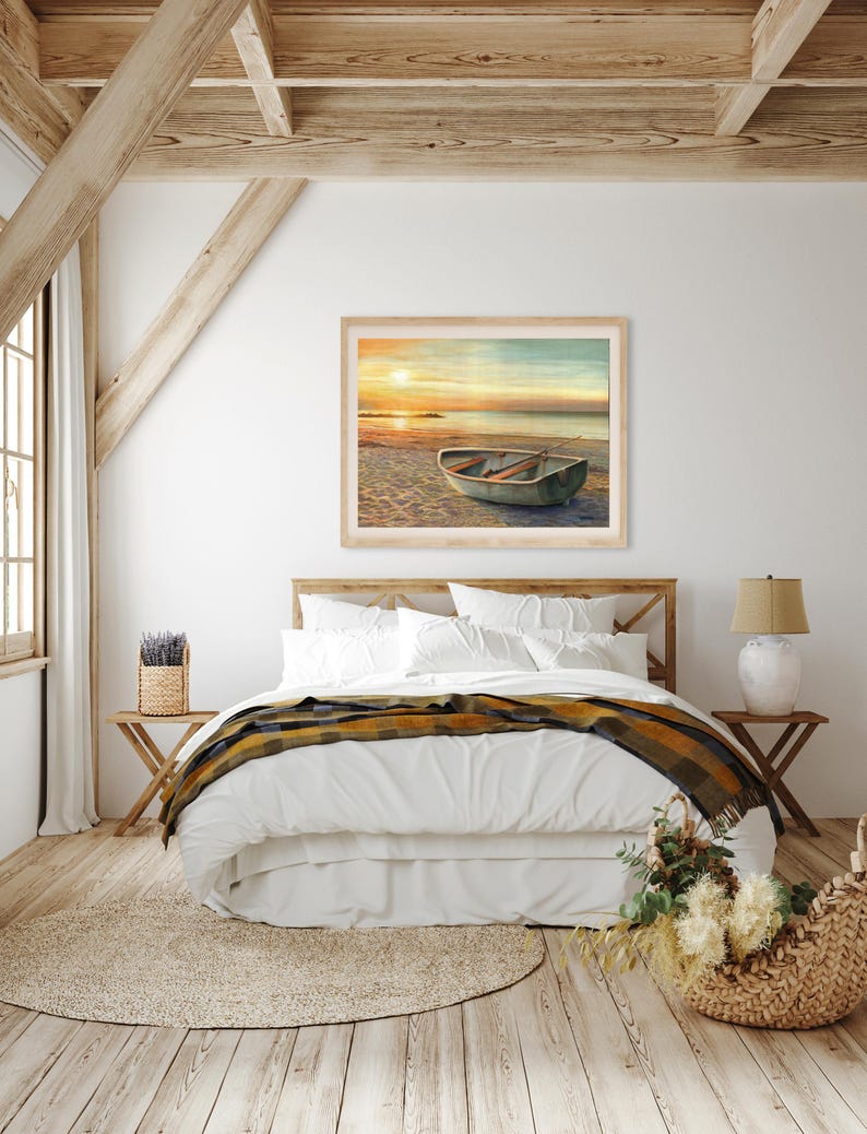 Op de afbeelding: Een rechthoekige ingelijste wandkunstprint met een schilderij van een kleine roeiboot die bij zonsondergang op een zandstrand ligt. De sc&egrave;ne toont een rustige kustlijn met een gloeiende oranje zon aan de horizon en houten roeispanen.