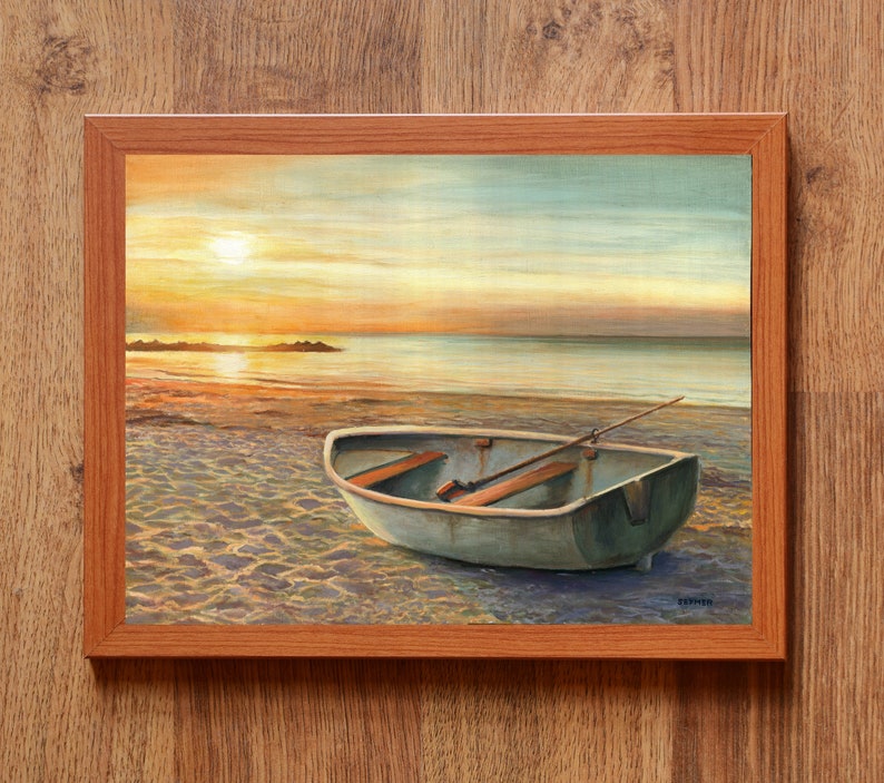 Op de afbeelding: Een ingelijst schilderij met een kleine roeiboot op een zandstrand bij zonsondergang. De sc&egrave;ne toont een kalme oceaan, een felle zon laag aan de horizon en zacht goudkleurig licht dat reflecteert op het water en de houten bankjes in de boot.