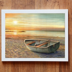 Op de afbeelding: Een ingelijst schilderij met een kleine roeiboot op een zandstrand bij zonsondergang. De sc&egrave;ne toont een kalme oceaan, een felle zon laag aan de horizon en een heldere lucht met zachte oranje en blauwe tinten. De boot heeft houten bankjes en een roeispaan.