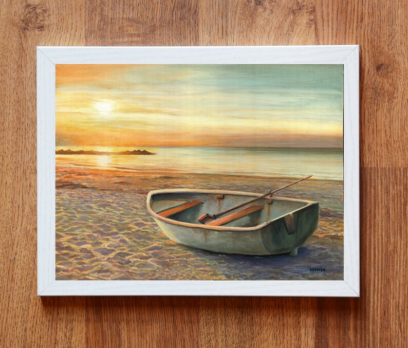 Op de afbeelding: Een ingelijst schilderij met een kleine roeiboot op een zandstrand bij zonsondergang. De sc&egrave;ne toont een kalme oceaan, een felle zon laag aan de horizon en een heldere lucht met zachte oranje en blauwe tinten. De boot heeft houten bankjes en een roeispaan.