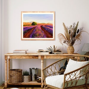 May include: A framed painting of a lavender field with a dirt road leading through the center. The field is a vibrant purple and the sky is a soft blue. The painting is in a wooden frame and is hanging on a white wall.