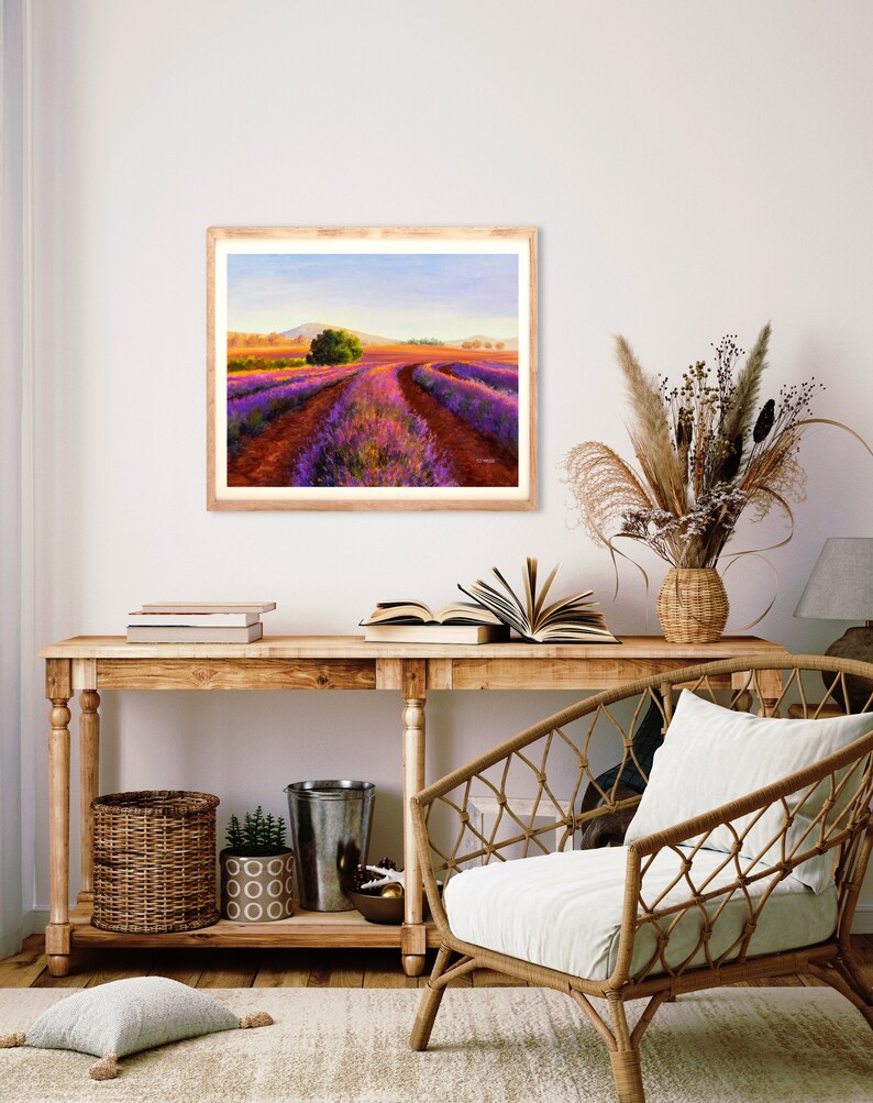 May include: A framed painting of a lavender field with a dirt road leading through the center. The field is a vibrant purple and the sky is a soft blue. The painting is in a wooden frame and is hanging on a white wall.