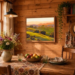 Peut inclure: Une peinture paysag&egrave;re encadr&eacute;e repr&eacute;sentant des collines verdoyantes sous un ciel de coucher de soleil chaud, expos&eacute;e sur un mur lambriss&eacute; au-dessus d'une table avec un vase en c&eacute;ramique, un bol de fruits et des assiettes en c&eacute;ramique.
