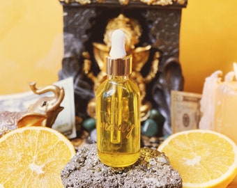 May include: A clear glass bottle with a dropper filled with a golden liquid. The bottle is sitting on a gray rock with orange slices and green leaves around it. The bottle has the word "money" written on it in gold lettering.