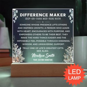 May include: A rectangular acrylic plaque with a dark green gradient background and white text reading DIFFERENCE MAKER, followed by a definition and the name Madison Smith. The plaque features floral illustrations and sits on a wooden LED base.