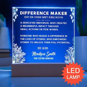 May include: A square LED acrylic lamp with a wooden base, featuring blue light and white text that defines a difference maker. The design includes floral accents on the sides and the custom signature name Madison Smith printed at the bottom.