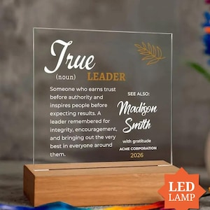 May include: A clear acrylic plaque set in a rectangular wooden base. The plaque features white and gold text defining a True Leader, including the name Madison Smith, the text Acme Corporation, and the year 2026, with a gold leaf graphic.