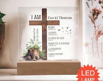 Pode incluir: Uma placa de acrílico transparente sobre uma base de madeira retangular com uma cruz castanha escura, uma ilustração de um tronco de árvore com folhagem verde e texto incluindo "I AM", "David Thomas", "Confirmed on 05-29-2024" e referências bíblicas.