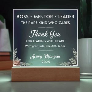 May include: A rectangular acrylic plaque with a dark green gradient background, mounted on a light wood base. The text reads: BOSS MENTOR LEADER THE RARE KIND WHO CARES Thank You FOR LEADING WITH HEART With gratitude, The ABC Team Avery Morgan 2025.