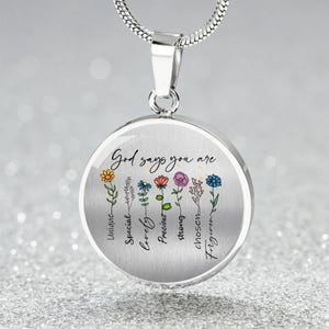 May include: A silver-colored pendant necklace with a round charm. The charm features colorful flowers and the words "God says you are" above the flowers, with additional words below them.