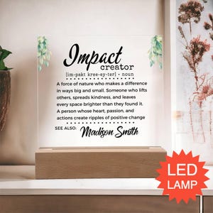 May include: A clear acrylic plaque with a wooden base featuring the printed text Impact creator, a phonetic pronunciation, and a definition of the term. The design includes green leaf illustrations on the top corners and the name Madison Smith.