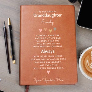May include: A tan leather-bound journal featuring the text TO OUR AMAZING Granddaughter Emily, followed by a poem about life chapters and love, ending with Your Signature Here. The cover includes small heart icons in various soft pastel colors.