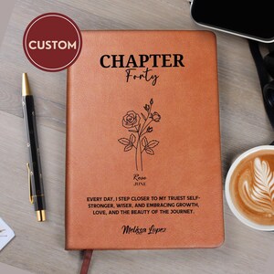 Peut inclure: Un journal en similicuir beige avec le texte noir "CHAPTER Forty", une illustration au trait d'une rose, le nom "Rose" avec "JUNE" en dessous, et la citation "EVERY DAY, I STEP CLOSER TO MY TRUEST SELF-STRONGER, WISER, AND EMBRACING GROWTH, LOVE, AND THE BEAUTY OF THE JOURNEY." avec le nom "Melissa Lopez" en bas.