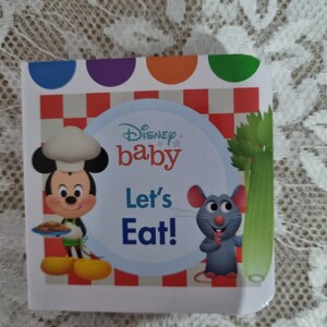 May include: A Disney Baby board book with a red and white checkered background. Mickey Mouse is dressed as a chef and holding a plate of food. A gray mouse is holding a stalk of celery. The book title is "Let's Eat!"