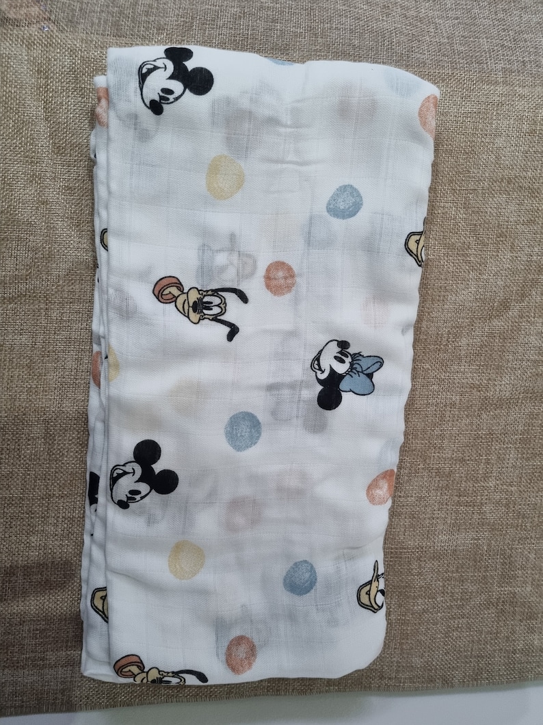 May include: A white muslin baby blanket with a repeating pattern of colorful polka dots and cartoon images of Mickey Mouse and Pluto.
