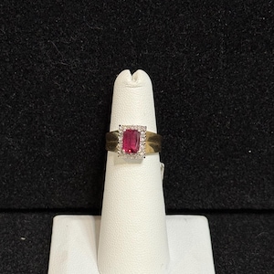 May include: A gold ring with a red gemstone set in a square frame of smaller white gemstones.