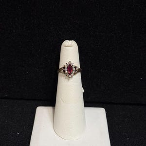 Peut inclure: Une bague en or avec une pierre ovale rouge entourée de petites pierres blanches.