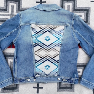 Peut inclure: Une veste en jean bleue avec un motif géométrique tissé sur le panneau arrière. Le motif est dans des tons de bleu, blanc et marron.