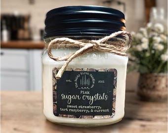 May include: A glass jar candle with a black lid and a twine bow. The label reads "Pink Sugar Crystals" with scent notes of sweet strawberry, tart raspberry, and currant. The candle is from The Salty Birch Candle Co.