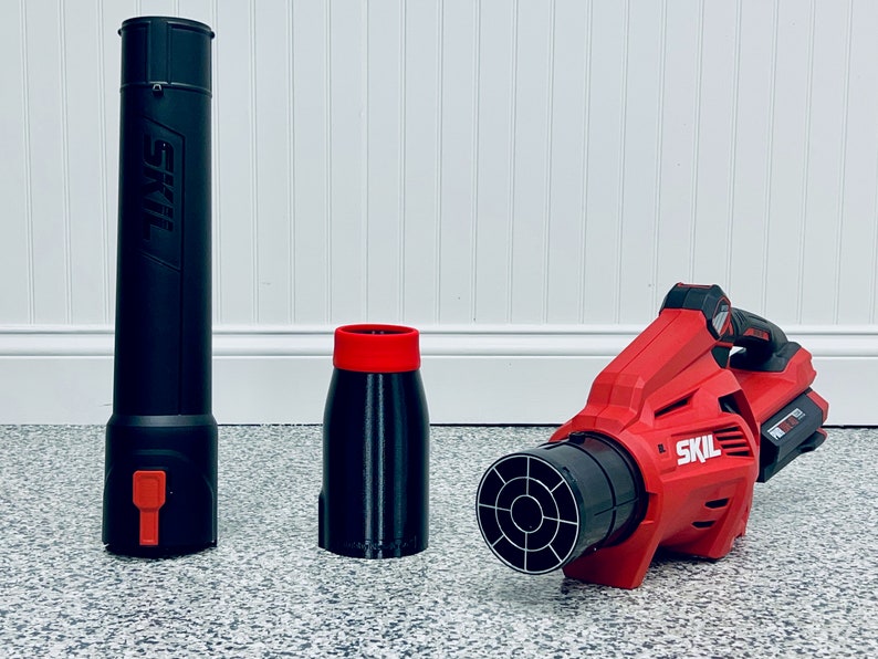 May include: A red and black cordless leaf blower with a black nozzle and a black and red extension nozzle. The leaf blower is made by SKIL.