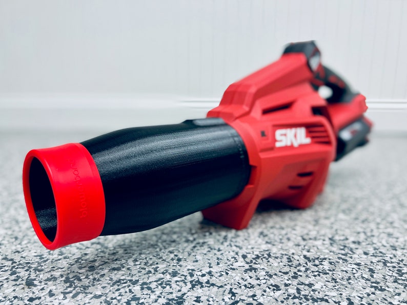 May include: A red and black cordless leaf blower with a black nozzle and a red tip. The blower has the word "SKIL" printed on the side.