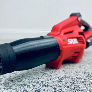 May include: A red and black cordless leaf blower with a black nozzle that says "blower" on it. The leaf blower is made by SKIL.