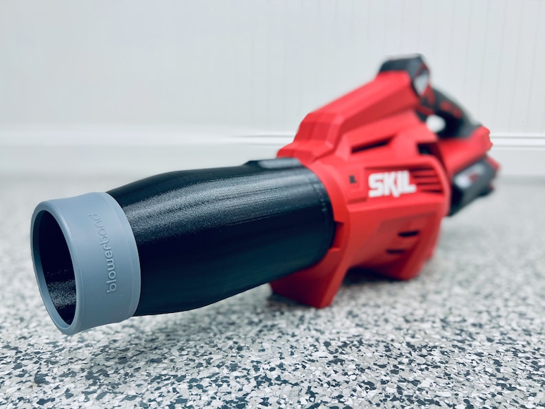 May include: A red and black cordless leaf blower with a gray nozzle. The nozzle has the word "Blowforce" printed on it. The leaf blower has the word "SKIL" printed on the side.