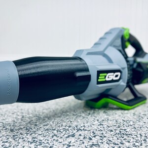 May include: A gray and black leaf blower with a green handle and the word "EGO" printed on the side. The blower has a black nozzle with a gray tip.