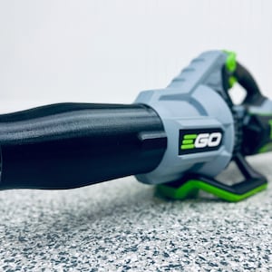 May include: A gray and green cordless leaf blower with a black nozzle. The blower has the word "EGO" printed on the side.