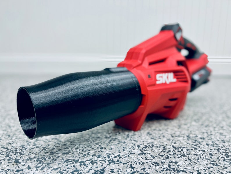 May include: A red and black cordless leaf blower with a black nozzle. The blower has the word "SKIL" printed on the side.